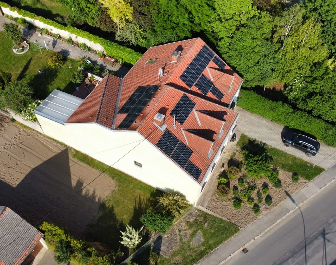 Luftaufnahme eines Einfamilienhauses mit Photovoltaikanlage auf mehreren Dachflächen, umgeben von Garten und Bäumen